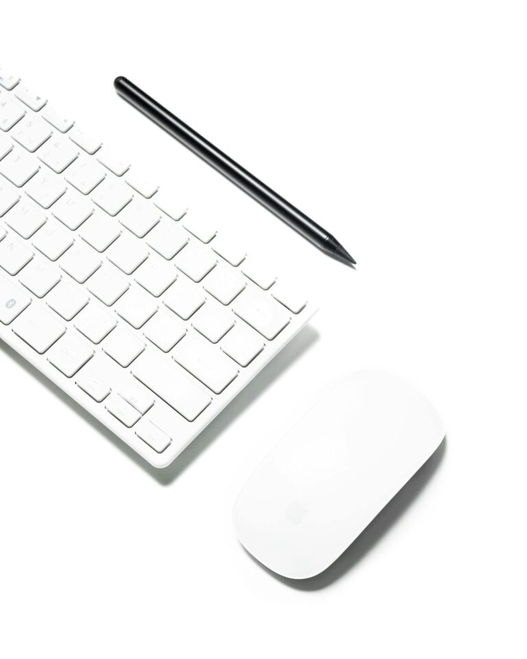 A clean and minimalist workspace featuring a wireless keyboard, mouse, and stylus on a white background.