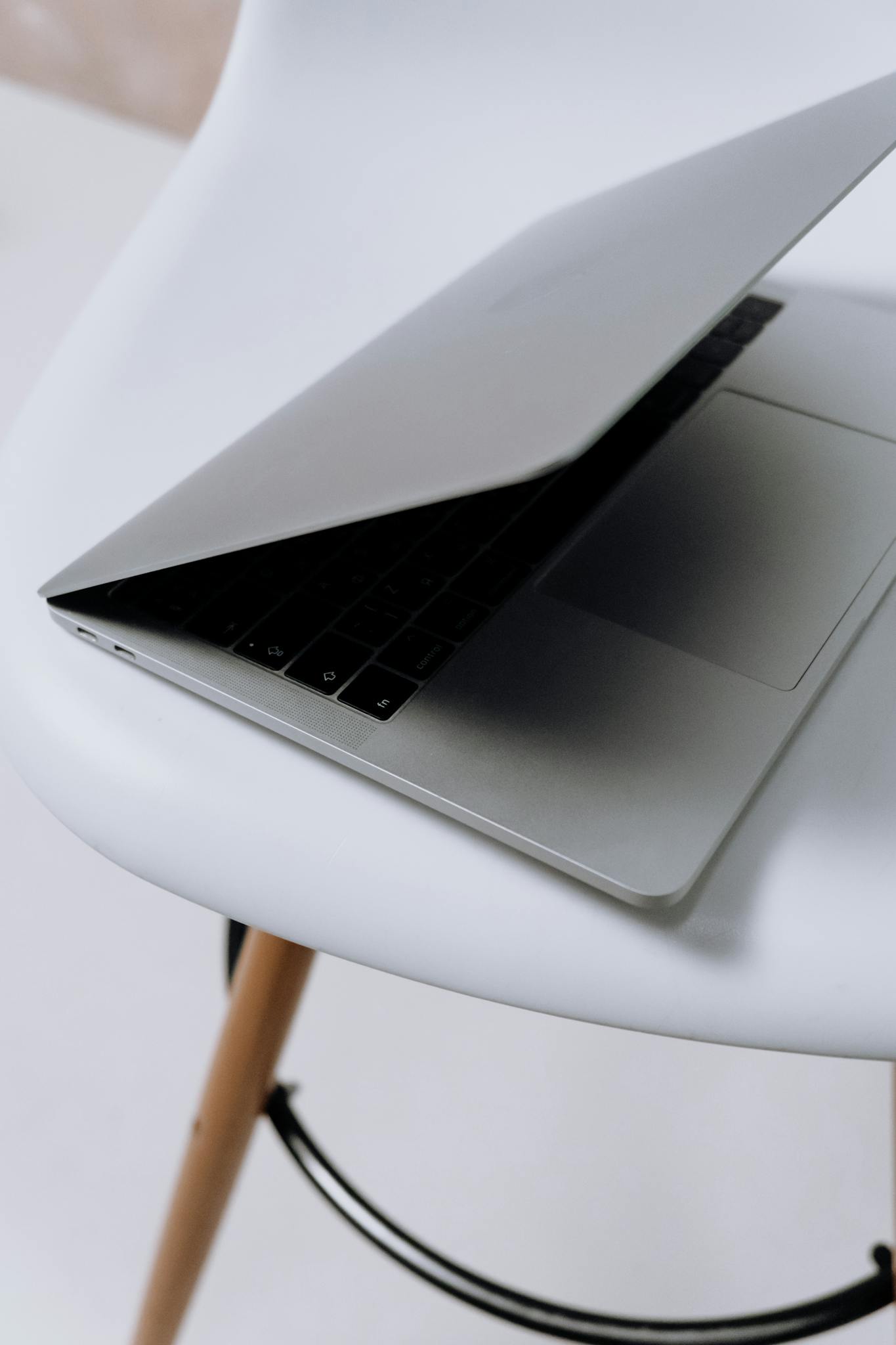 Sleek laptop half-open on a stylish white chair, perfect for modern office concepts.